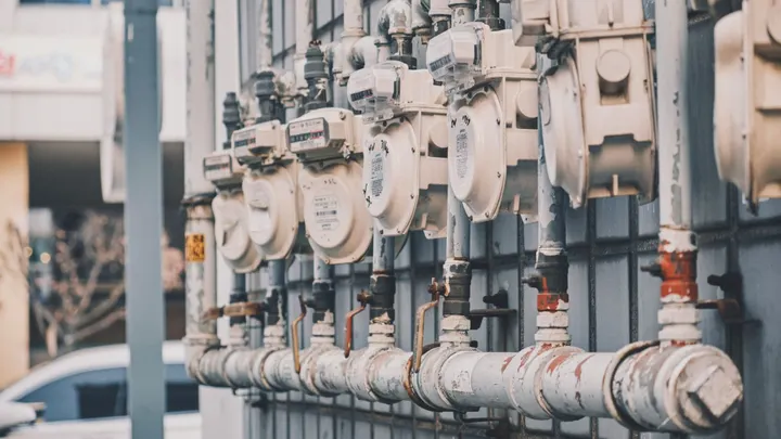 A row of residential water meters and connected service pipes mounted along the exterior of a building.