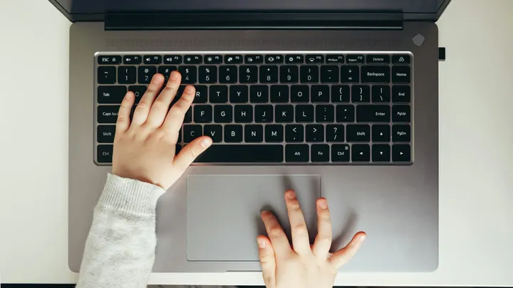 Close-up of a child’s hands using a laptop keyboard and trackpad.