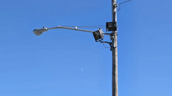 Two surveillance cameras mounted on a utility pole against a clear blue sky.