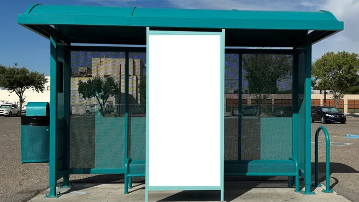 Teal Las Cruces bus shelter with benches and a large blank display panel in the center under a blue sky.