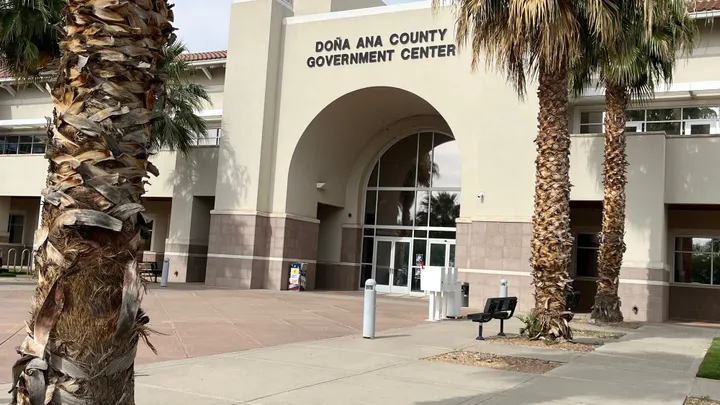 The Doña Ana County Government Center in Las Cruces, framed by palm trees near the main entrance.