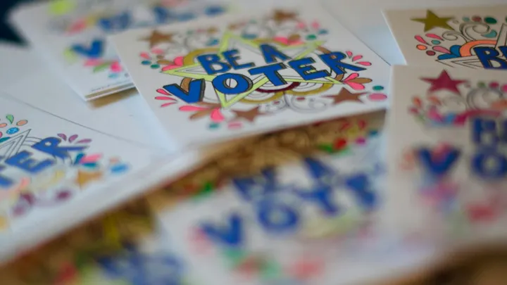 Colorful “Be a Voter” cards are spread across a table, with one card in sharp focus and others blurred in the foreground and background.