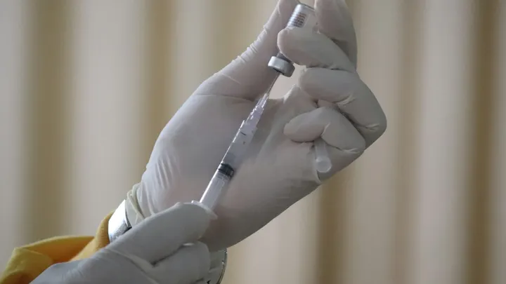 Gloved hands draw vaccine from a vial into a syringe.
