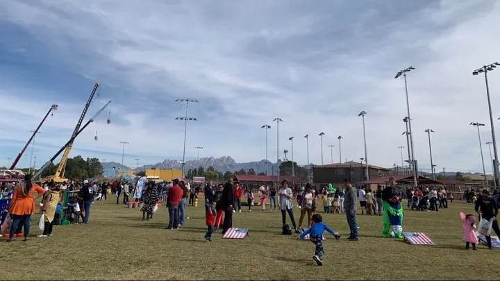 Families and children gather on Maag Field in Las Cruces during a Great Pumpkin Candy Drop event, with cranes, games and the Organ Mountains in the background.