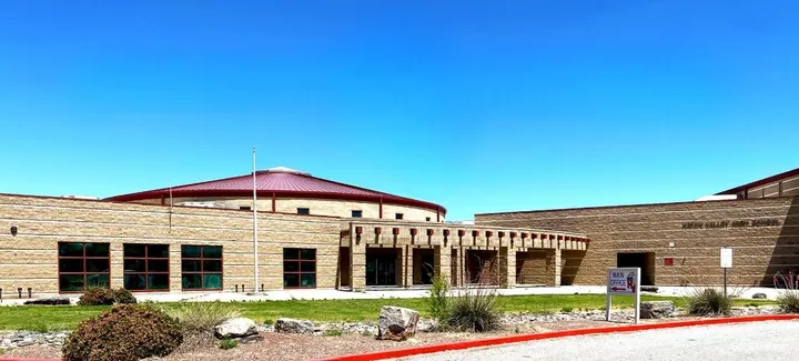 Exterior of Hatch Valley High School, showing the main entrance, tan brick buildings, red metal roof and landscaped grounds.