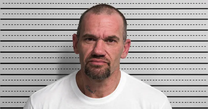 Booking photo of Kurtis Allan Dale, wearing a white shirt, with short hair and a goatee, against a height-measurement backdrop.