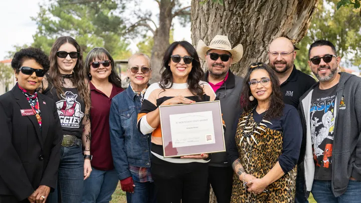 Amanda Nunez, center, holds her framed 2026 “A” Mountain Staff Award while posing with eight people outdoors at New Mexico State University.