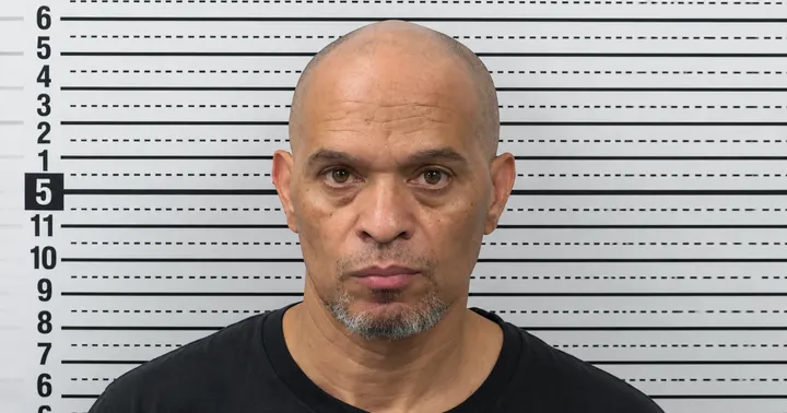 Mugshot of Ronald C. Jackson, a bald man with a short gray goatee wearing a black shirt, photographed against a correctional facility height chart.