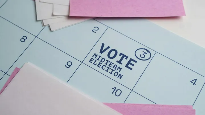 Close-up of a blue calendar with “VOTE MIDTERM ELECTION” printed on one date, surrounded by pink and white papers.