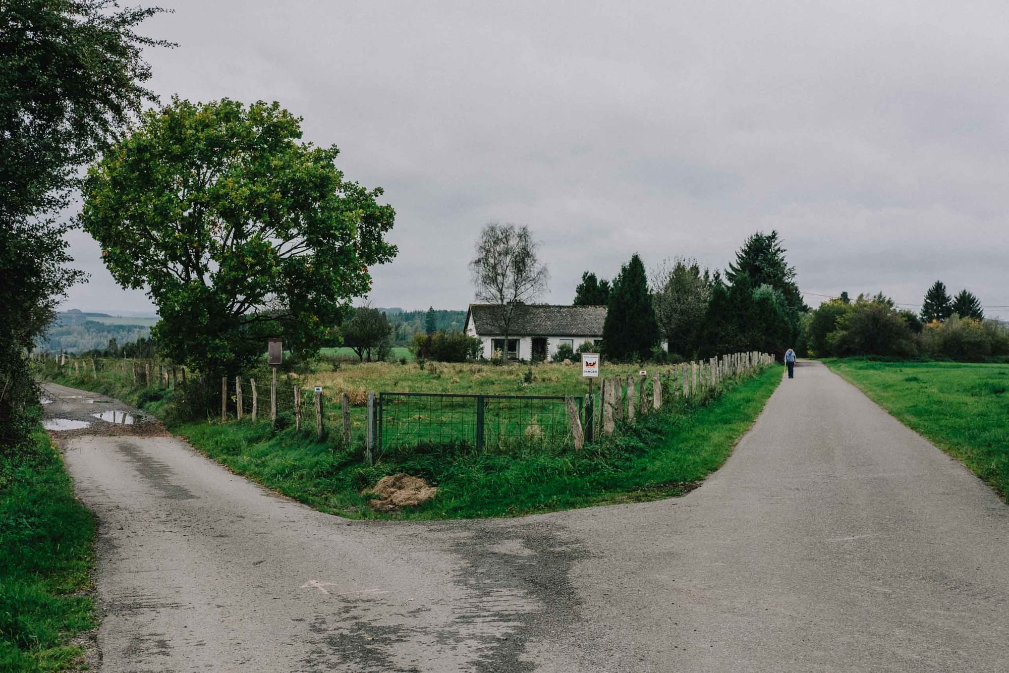 Rural crossroads with a farmhouse and walking figure in the Belgian countryside photographed with the Fujifilm XF35mm f2