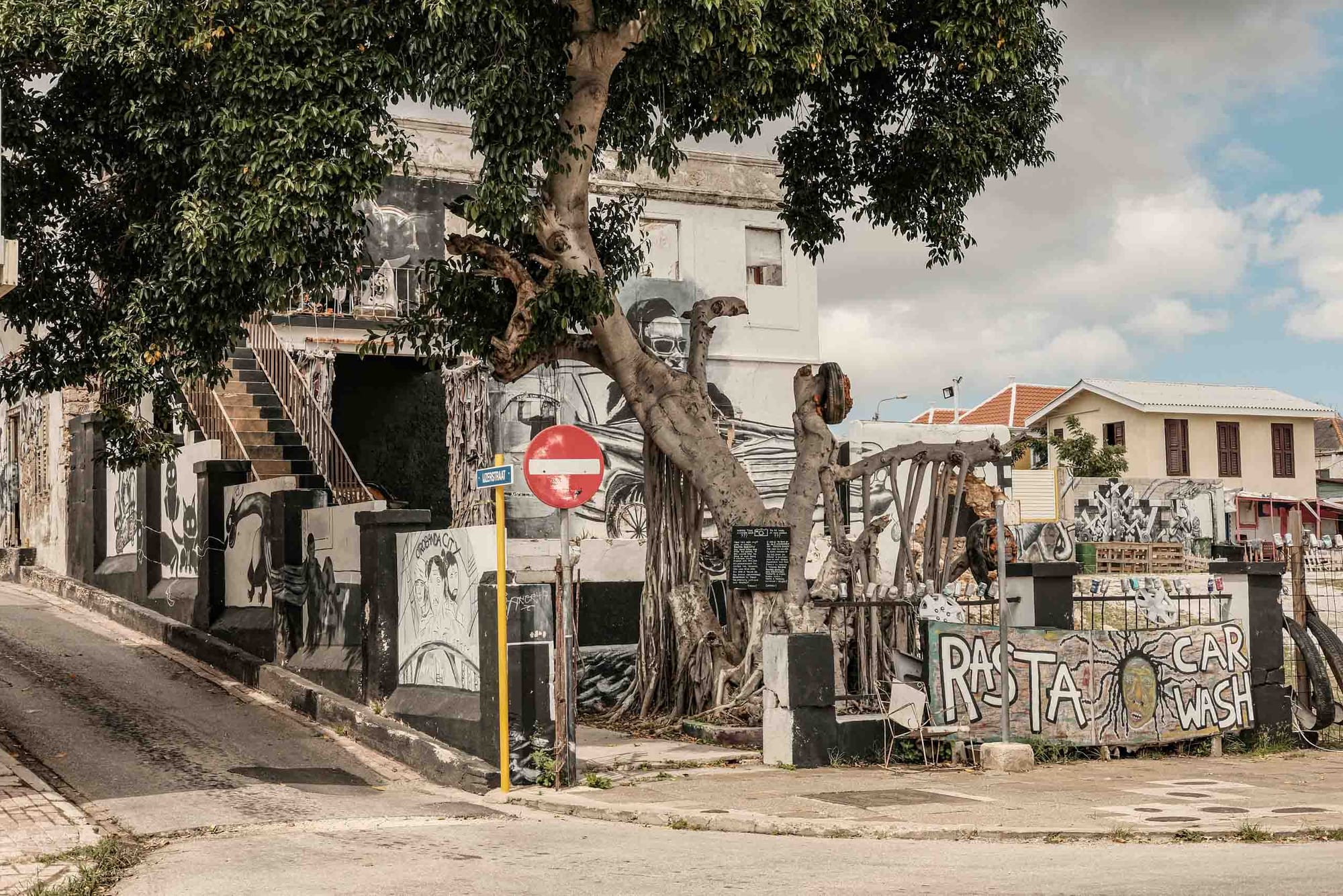 Street corner with murals and a large tree in Willemstad, Curaçao photographed with the Fujifilm XF35mm f2 at f8 during a daytime walk through the city