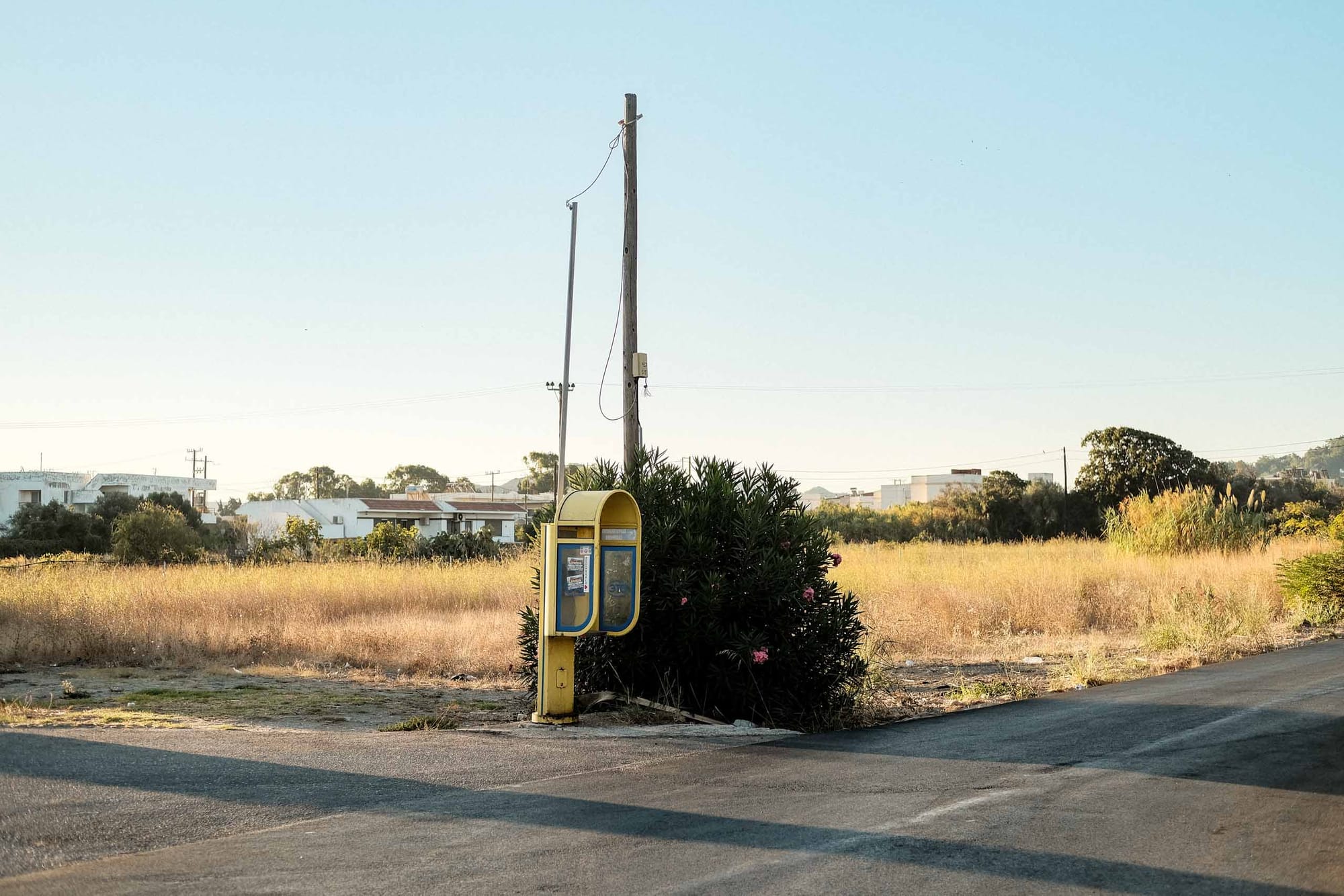 Telephone booth beside a quiet roadside in Kremasti, Greece photographed with the Fujifilm XF35mm f2 at f2.5 during morning golden hour