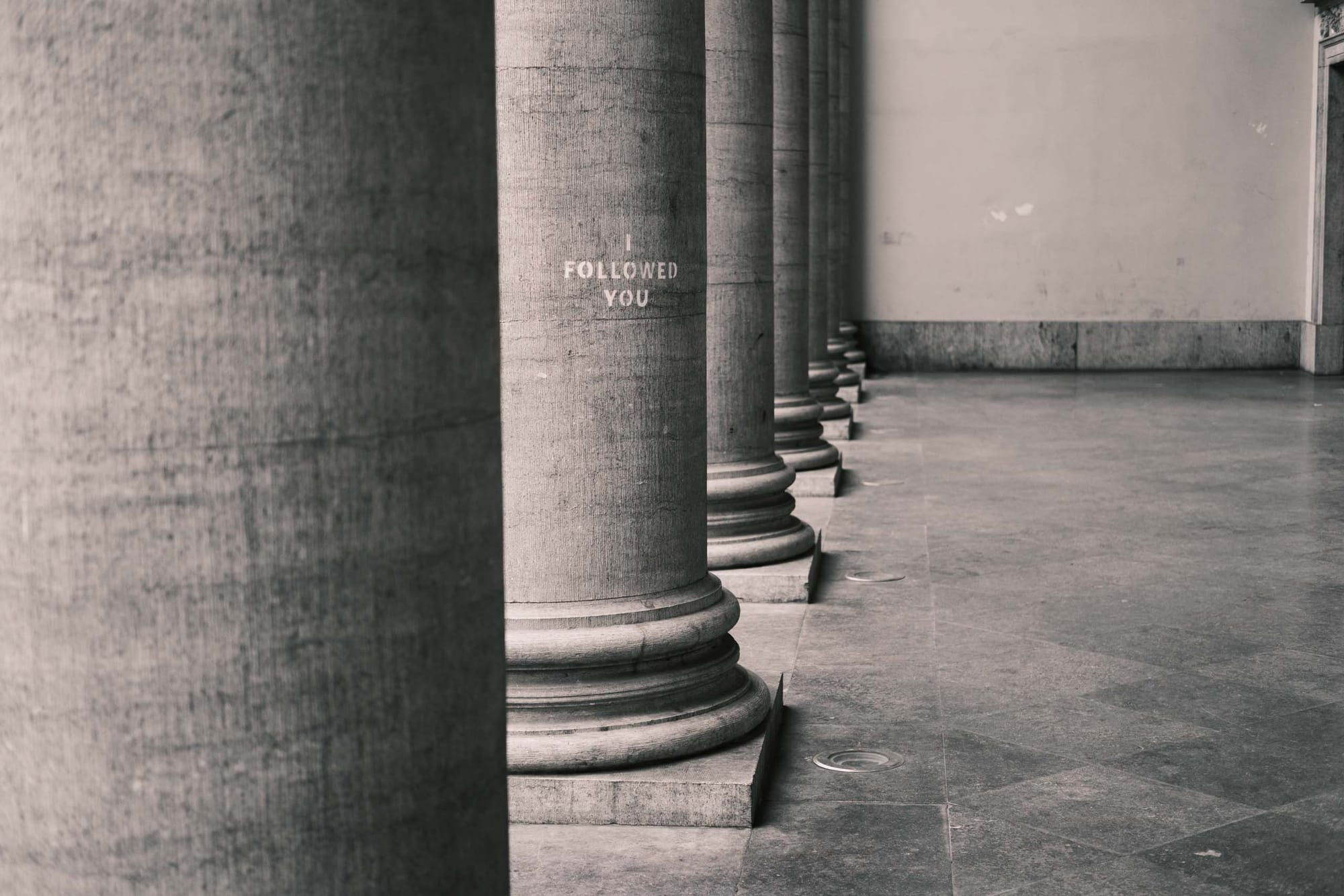 sample image with Fujifilm XF35mm f2 at f2 — Ghent, Belgium — stone columns with faded ‘I FOLLOWED YOU’ text in a quiet corridor