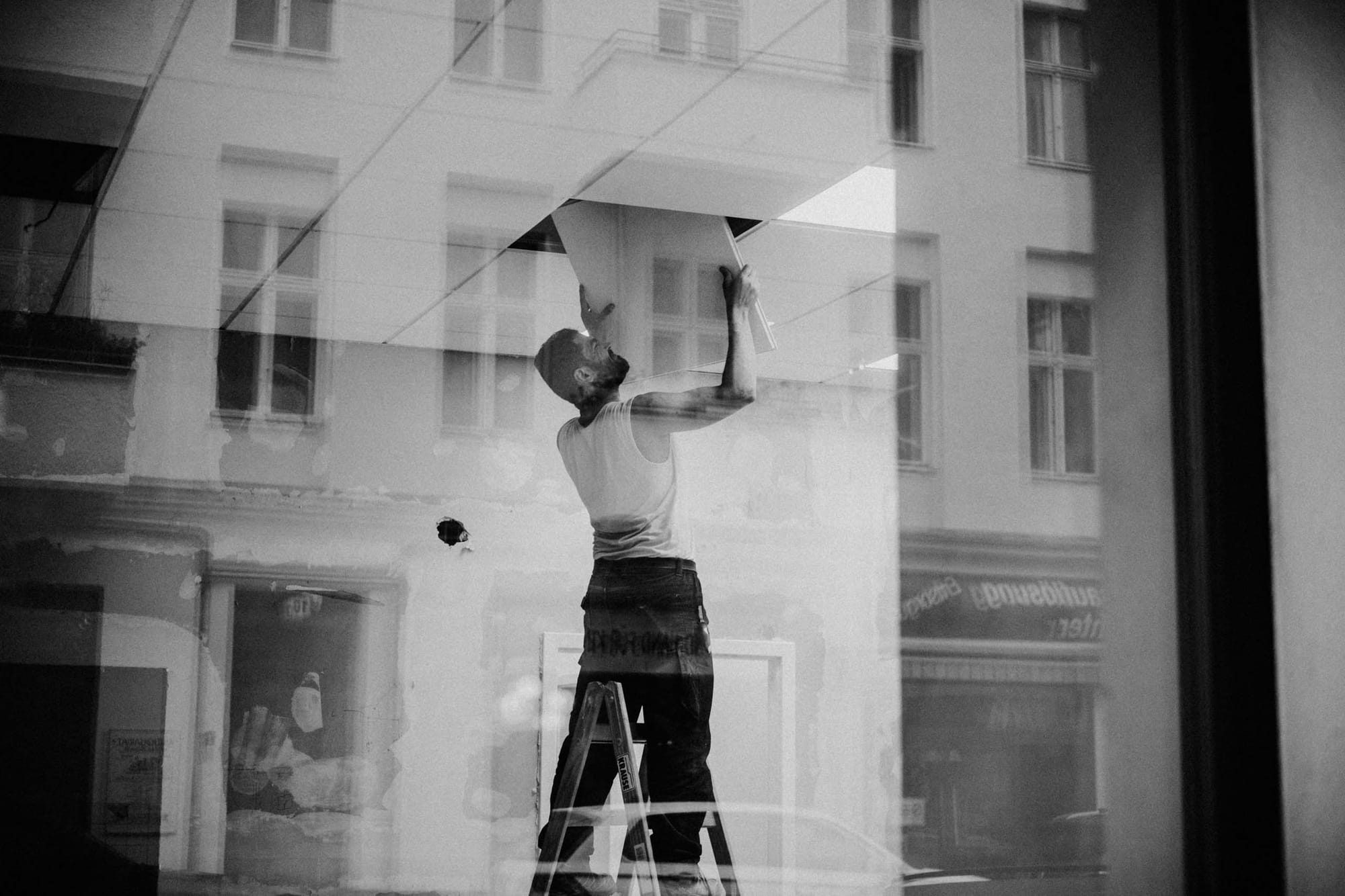 sample image with Fujifilm XF35mm f2 at f2 — Berlin, Germany — worker on a ladder reflected through layered storefront windows