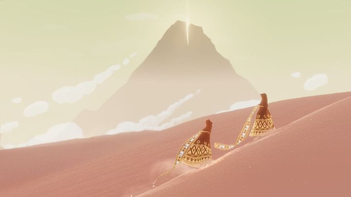 A screenshot from Journey shows two characters walking up a hill made of sand, with a giant mountain visible in the distance.