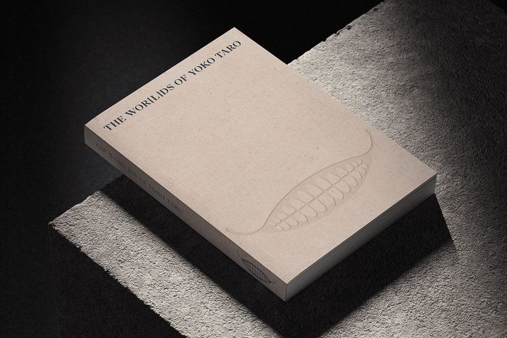 An official photo shows the book The Worlds of Yoko Taro on a gray stone.