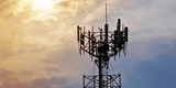 Silhouetted telecommunications tower with antennas against a cloudy sunset sky.