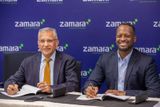 Sundeep Raichura and Frank-Astère Ndiyo Butoyi seated at a desk in front of a blue Zamara-branded backdrop while signing documents.