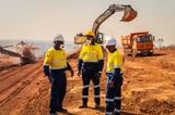 Nimba Mining Company engineers in high-visibility uniforms reviewing operations at an active bauxite extraction site with heavy machinery in the background.