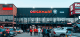 Exterior view of a Quickmart supermarket branch with parked vehicles and shoppers walking in front of the storefront.