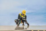 A Sun King technician wearing a yellow hard hat, safety harness, and gloves crouches while installing solar panels on a rooftop.