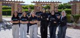 The NoorNation team posing together outdoors in black branded t-shirts and shirts with arms crossed, in front of a garden setting with wooden pergolas.