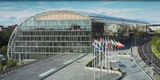 Exterior view of the European Investment Bank (EIB) East Building headquarters in Luxembourg, featuring a large curved glass facade and flags of European Union member states flying out front.