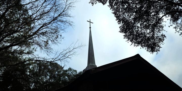 A church steeple amongst trees with part of the roof in view.