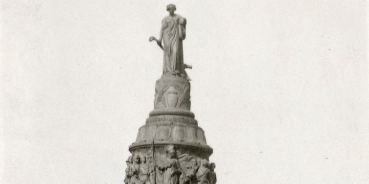 Black-and-white photograph of the top of the Arlington Confederate Memorial. A robed bronze woman stands on a tall pedestal above a circular frieze of crowded sculpted figures
