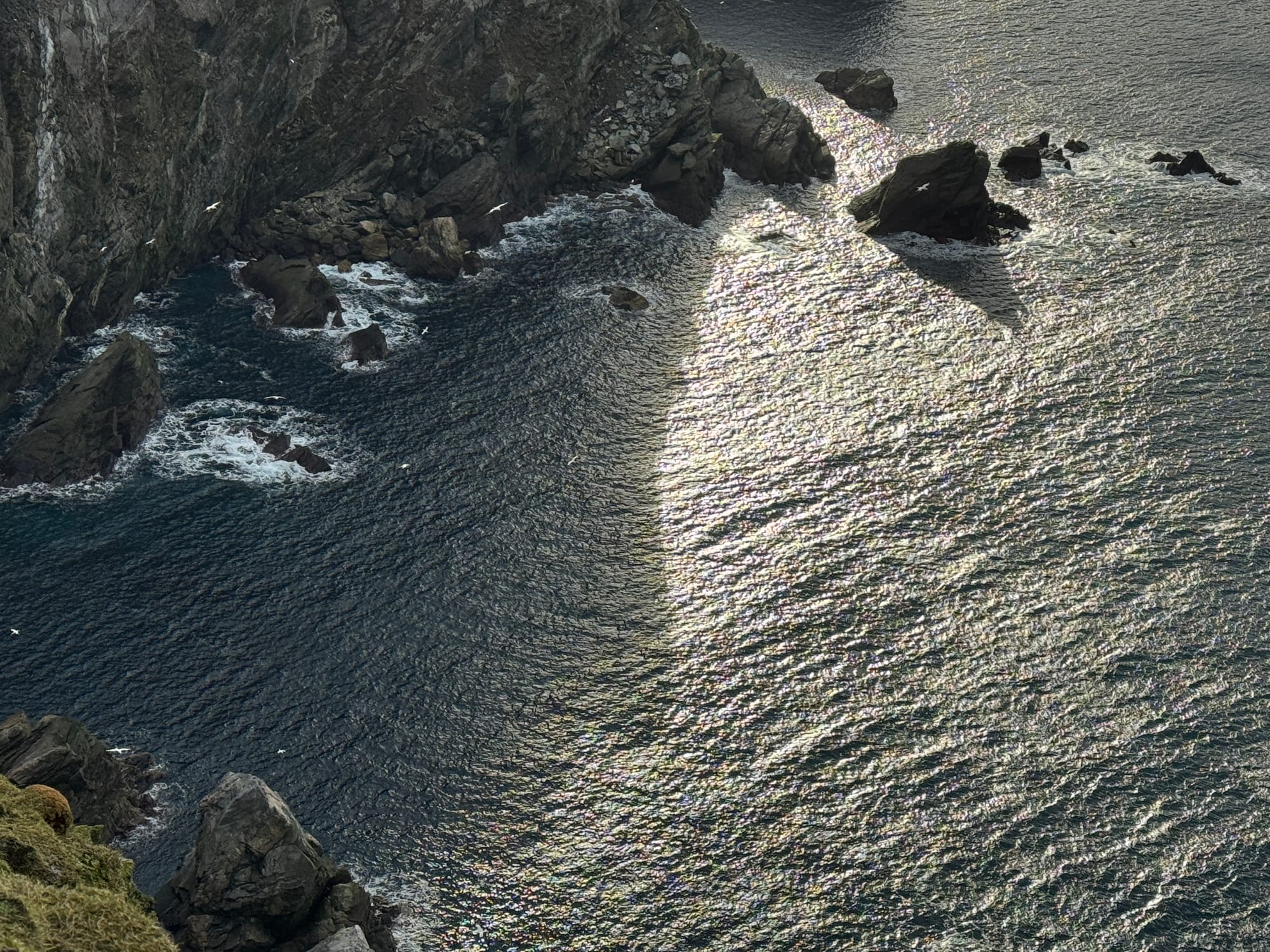 looking down onto ocean and sea stacks casting shadows from the height of a cliff's edge