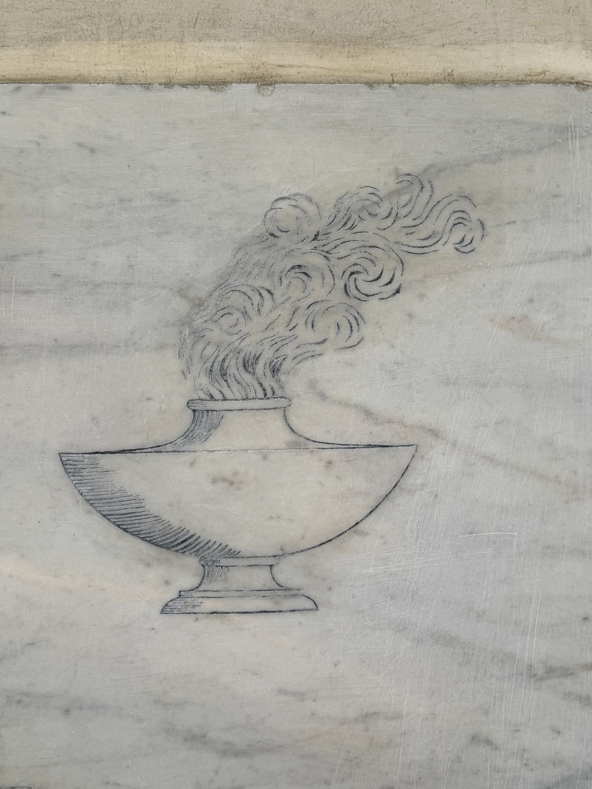 A close-up photograph of an engraving on a marble surface depicting a classical oil lamp. 