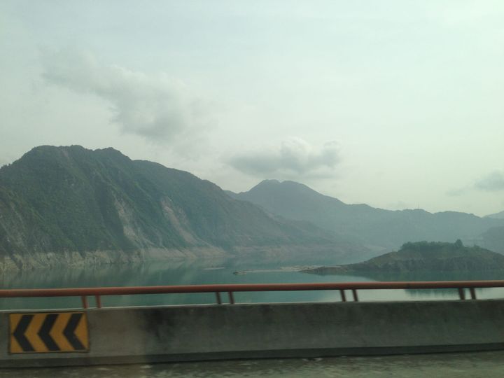 a road built suspended upon lake with views of hills and grey sky 