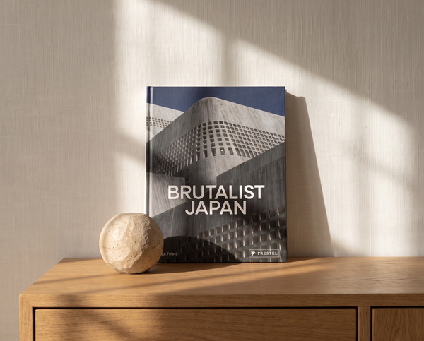 Hardcover book Brutalist Japan by Paul Tulett, Prestel, styled on an oak surface against a linen wall, minimal editorial interior styling.