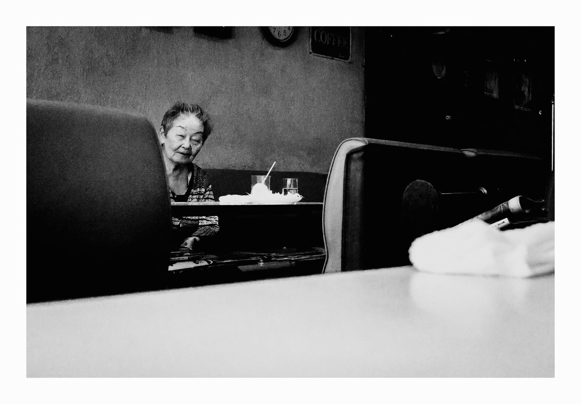 Old Japanese lady peeking from behind seats, Kyoto kissaten, black and white fine art photo.