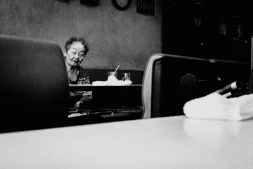 Old Japanese lady peeking from behind seats, Kyoto kissaten, black and white fine art photo.