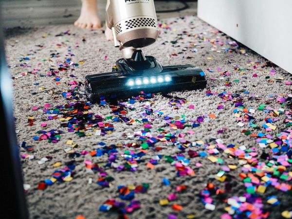 A cordless vacuum cleaner on a carpet covered in coloured confetti