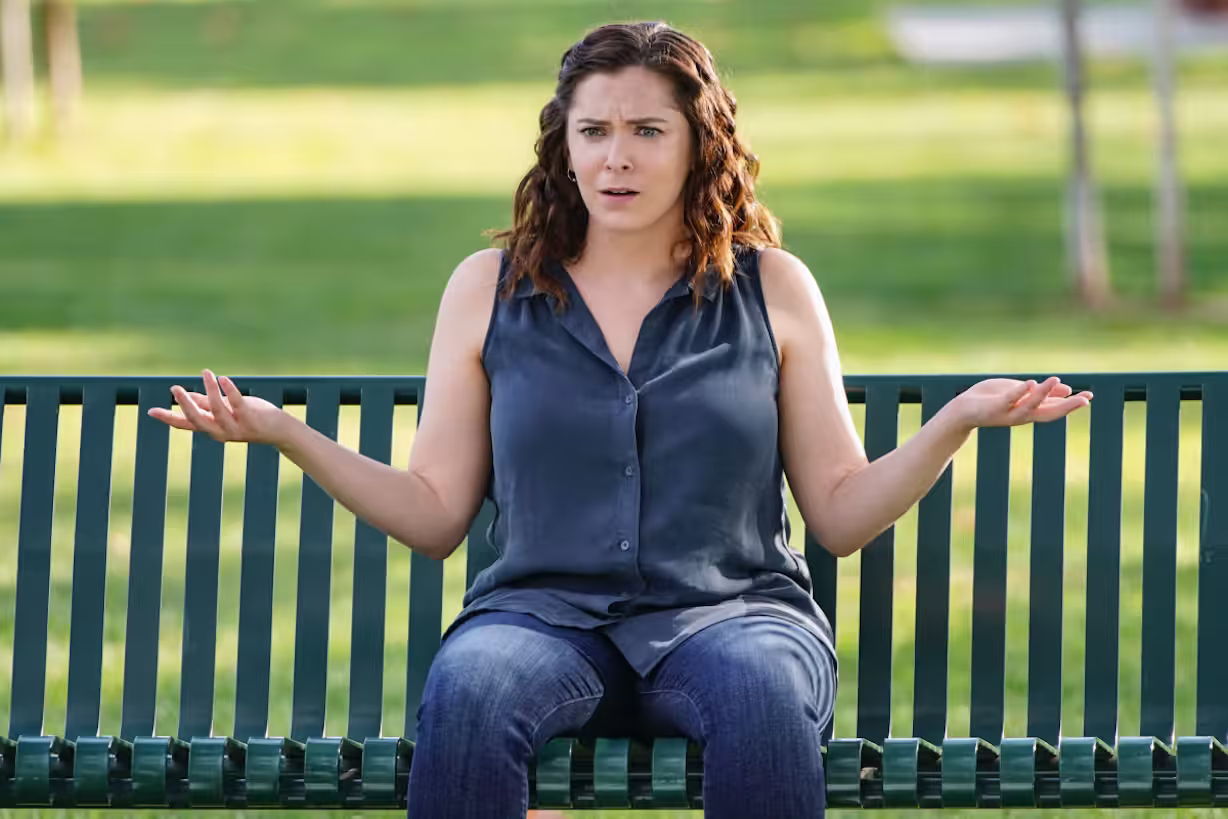 Rachel Bloom as Rebecca Bunch sitting on a bench in a sunny park looking incredulous