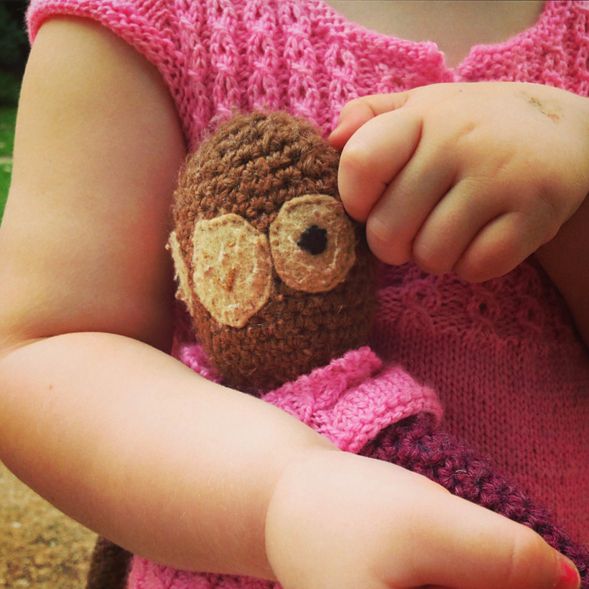 Marlowe and her favorite stuffed monkey wearing matching handknit pink dresses.