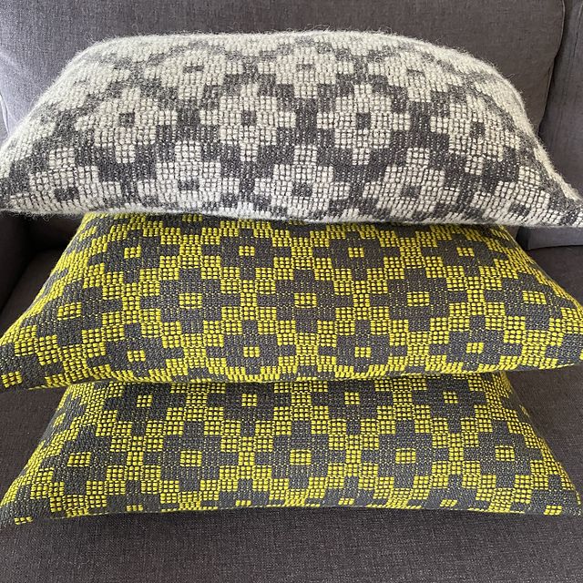 a stack of three pillows with woven covers. the top pillow is cream and grey, while the bottom two are chartreuse and grey. all three feature a cross motif.