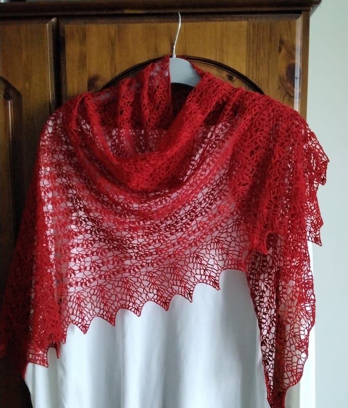 A red crocheted lace shawl hangs delicately draped from a coat hanger.