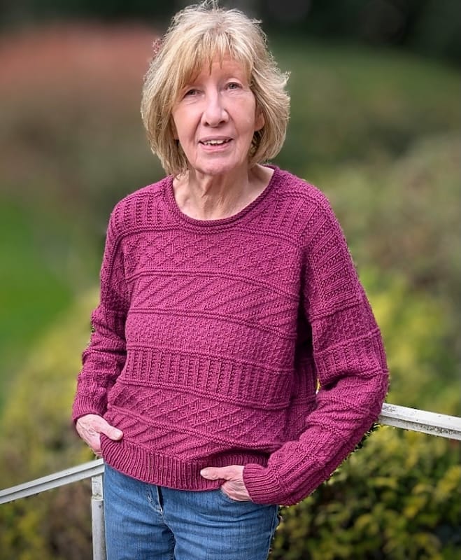 A knitter smiles at the camera in a rich magenta textured sweater.
