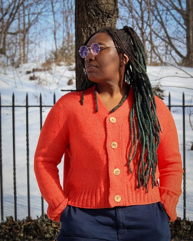 A crafter stands in a glowing orange handknit sweater they made.