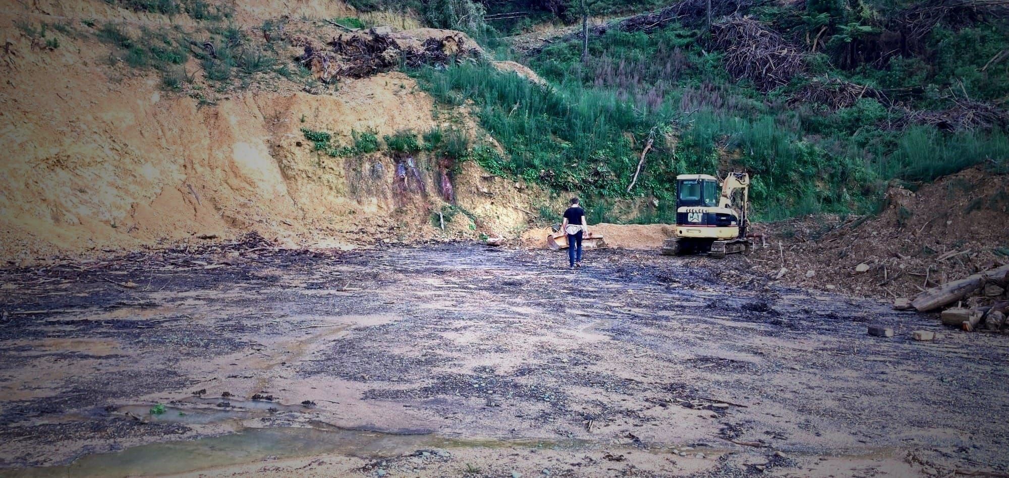 Xander walking on an empty skid site with a digger, lots of mud and a big mess!