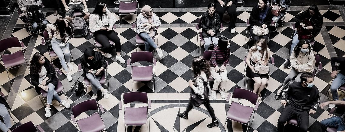 Jongeren zitten in een kring op een geblokte marmervloer tijdens een politiek debat in een burgerzaal.