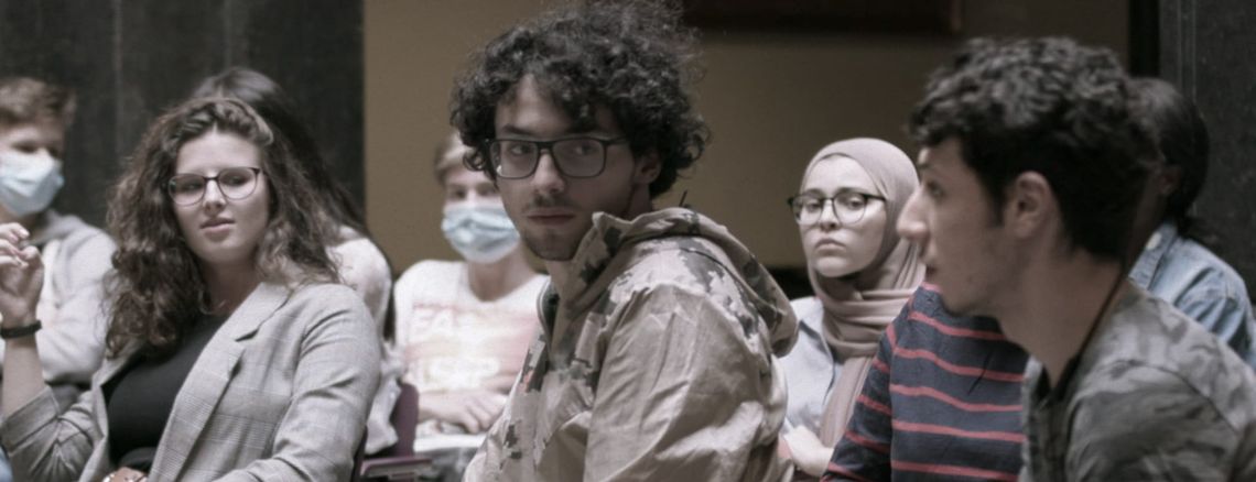 Close-up van leerlingen die aandachtig luisteren tijdens een debat in een burgerzaal.