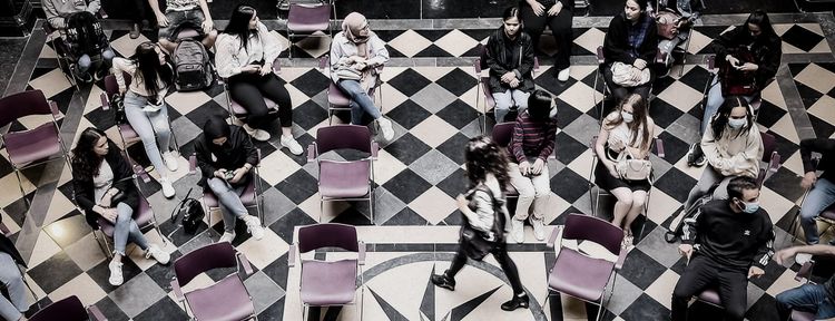 Jongeren zitten in een kring op een geblokte marmervloer tijdens een politiek debat in een burgerzaal.