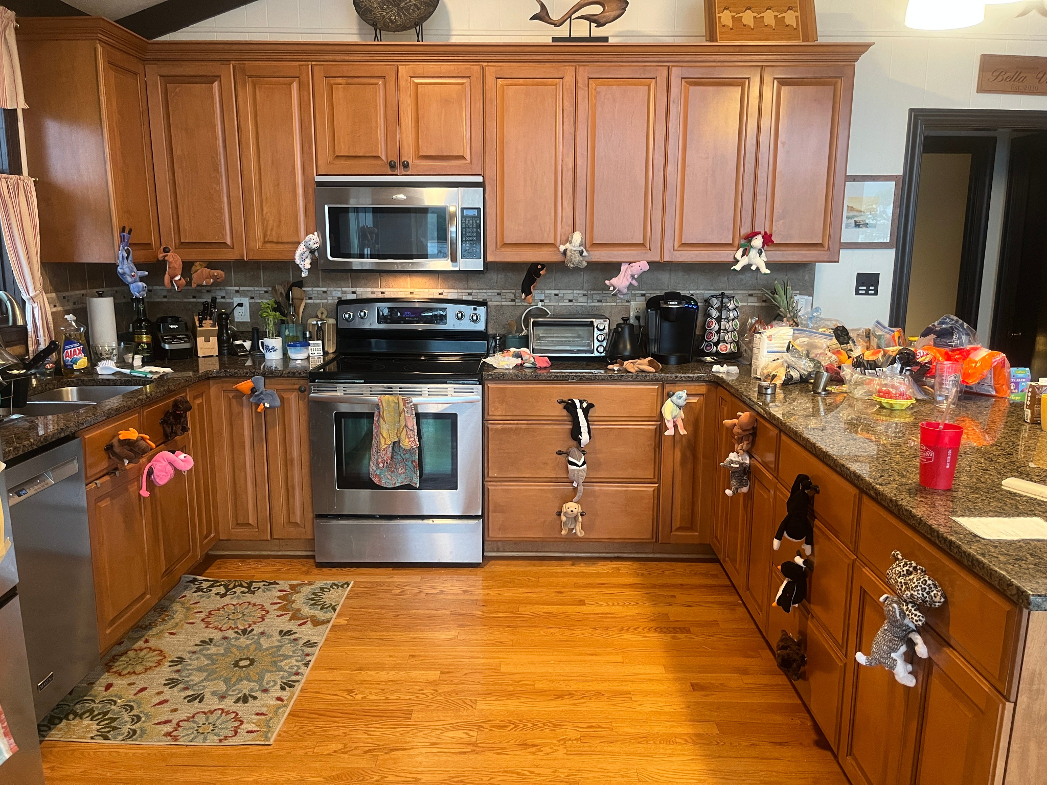 A kitchen with wood cabinets and dark granite countertops, decorated with dozens of Beanie Babies, including dogs, cats, a flamingo, and a leopard, all clipped or hung from cabinet and drawer handles.