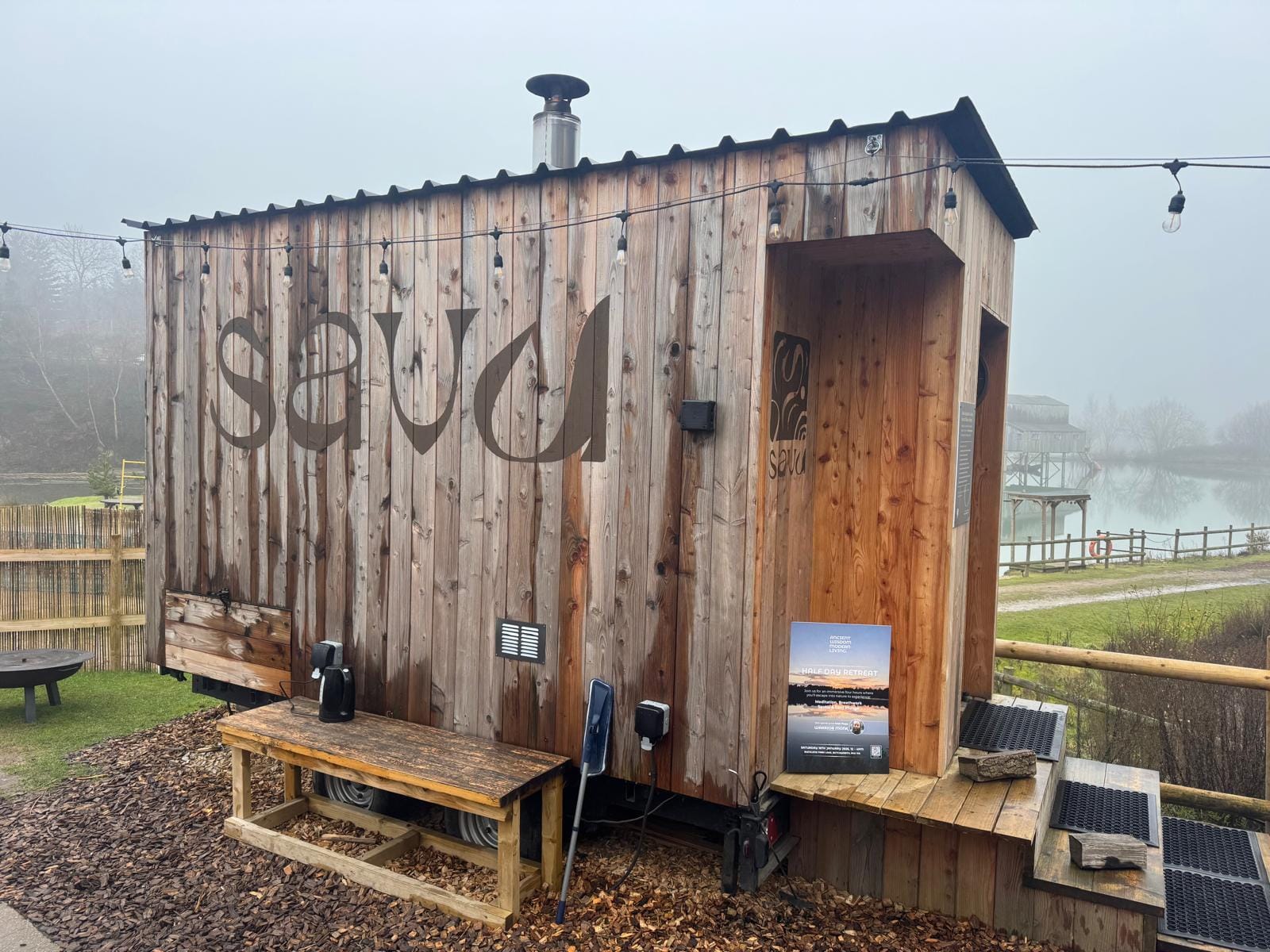 Side view of Savu sauna cabin showing recessed entrance area and chimney at Buckland Park Lake.