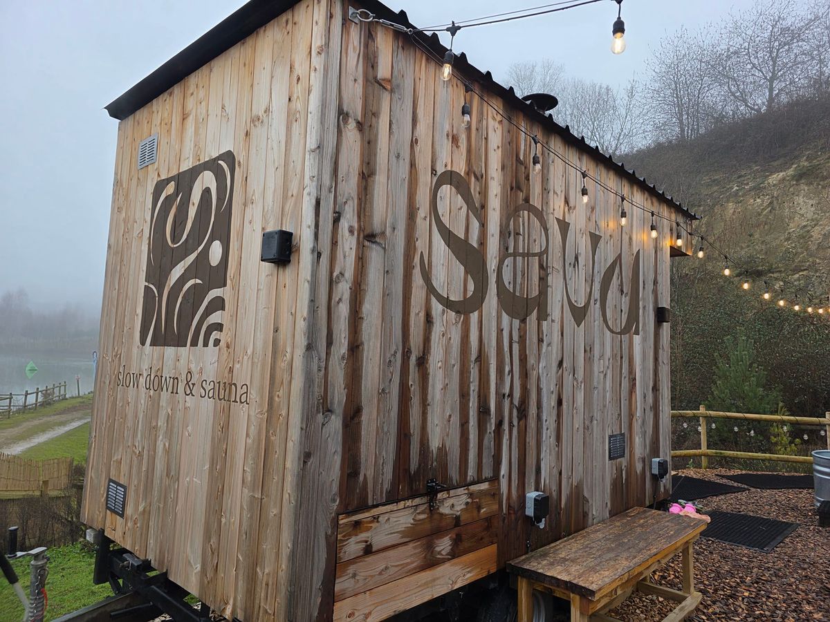 Exterior of Savu sauna cabin at Buckland Park Lake in Surrey with string lights and plunge area nearby.