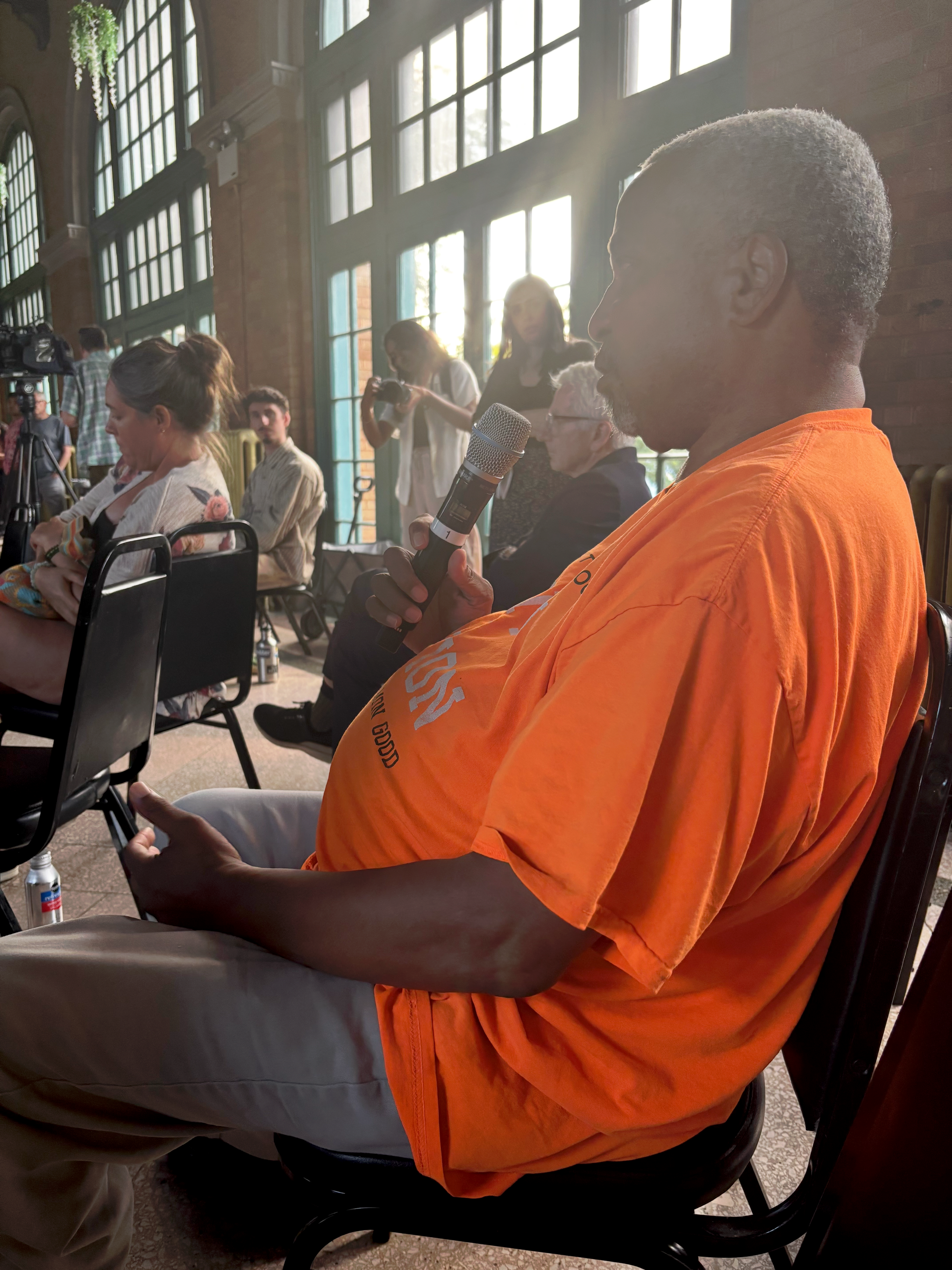 A man in a bright orange shirt and pants, Reverend Booker Vance, presents a question for panelists.